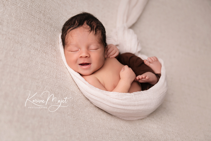 meilleure photo de naissance garçon dans un cocon blanc en train de sourire Karine Majet