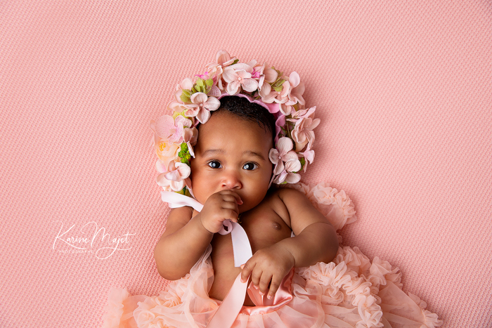 portrait d'un bébé fille suçant son pouce avec un bonnet de fleur Karine Majet