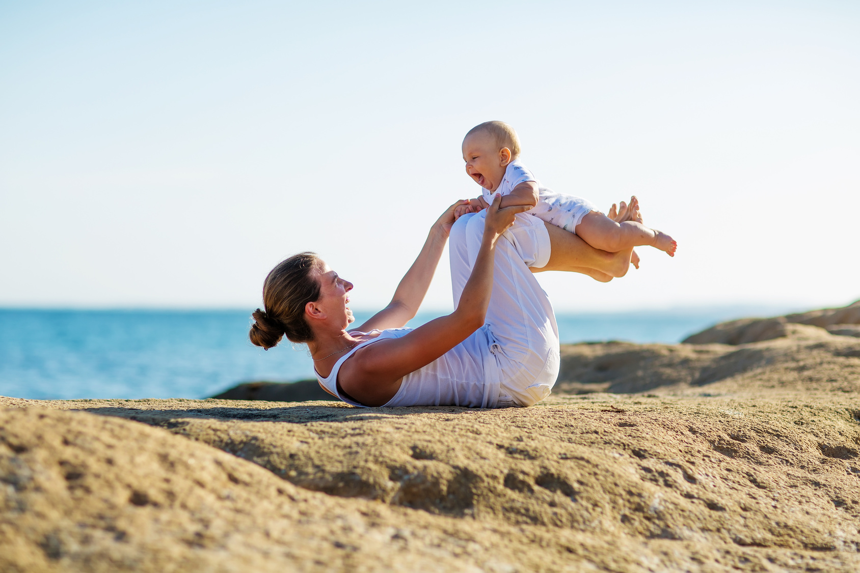 une maman fait du yoga avec son bébé en bord de mer