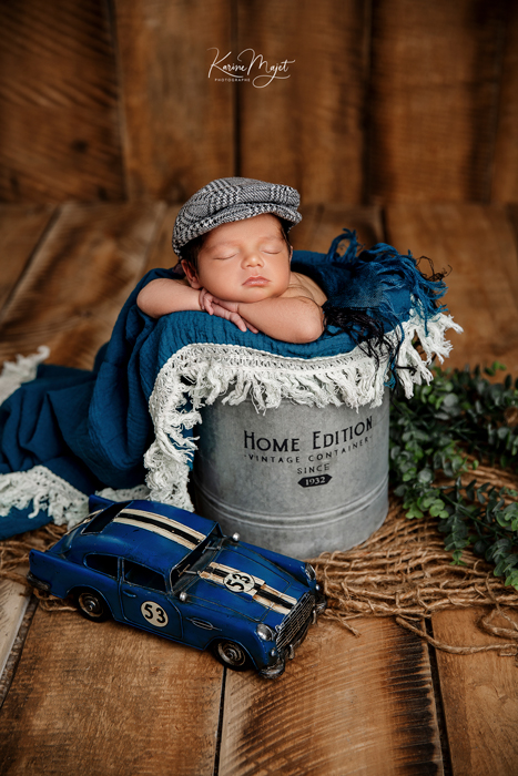 photo de naissance nouveau-né dans un seau avec une casquette et une voiture bleue karine majet photographe