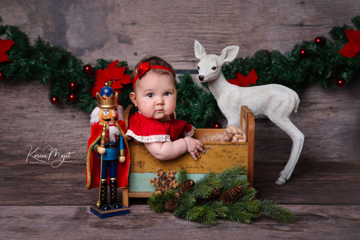 décor de noël avec une petite fille habillée en rouge, un casse-noisette et un faon à côté d'elle sur un fond en bois