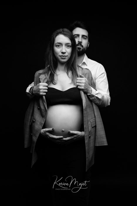 photo stylisée de grossesse, maman avec une veste extra large portée sur les épaules et le papa derrière karine majet