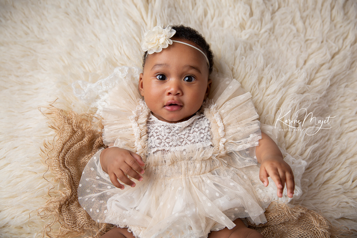 portrait bébé en retouche standard petite fille allongée sur le dos avec une robe bohème crème Karine Majet