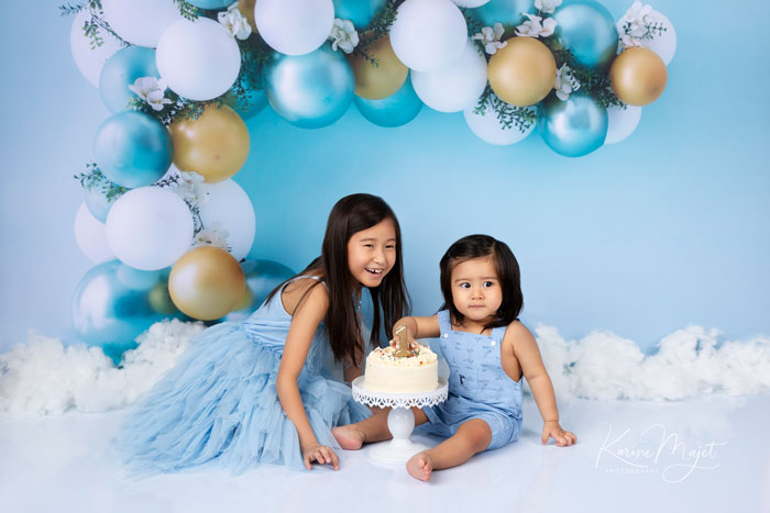 shooting anniversaire un an avec la grande sœur dans un décor avec des ballons bleus