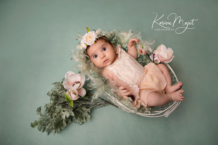 séance photo naissance petite fille dans un panier blanc avec des fleurs roses t un fond vert eau karine majet photographe