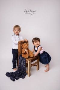 frère et sœur en train de jouer avec un ours sur une chaise en bois