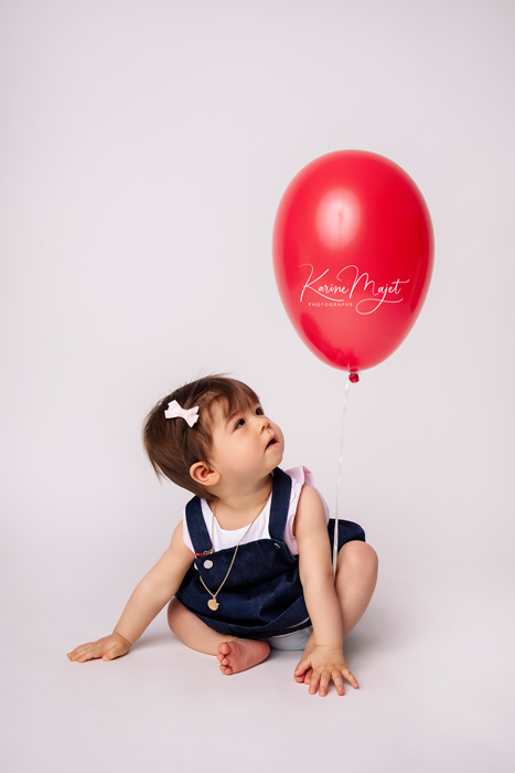 petite fille de huit mois assise et jouant avec un ballon rouge Karine Majet