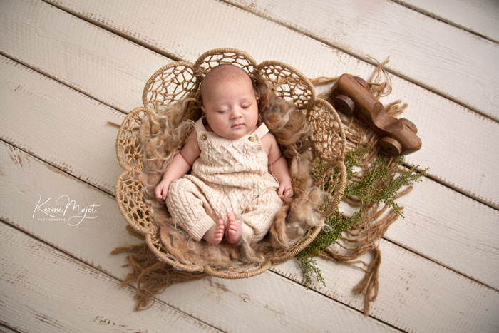 séance photo naissance sur le thème bohème avec une petit garçon endormi dans un panier rond sur un tapis en toile de jute
