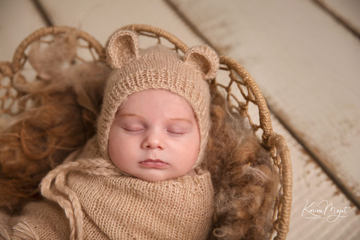 photo de naissance où le garçon est emmailloté dans un lange beige avec un bonnet aux oreilles d'ours