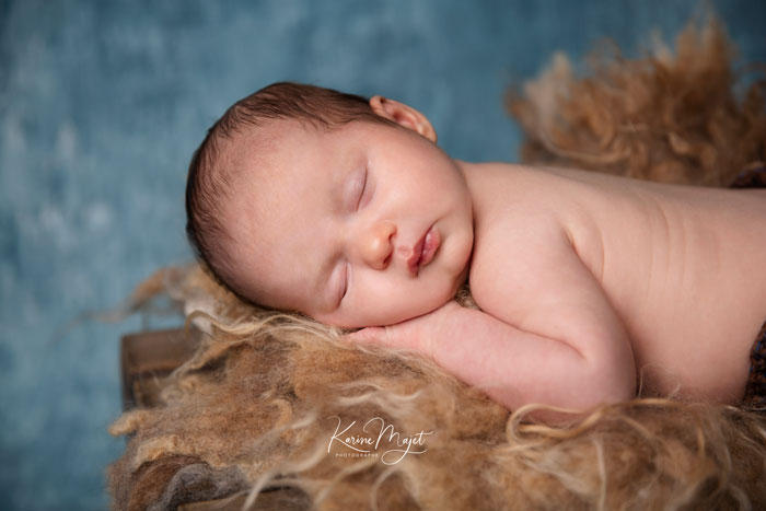 bébé garçon endormis sur une couverture en laine marron et sur fond bleu