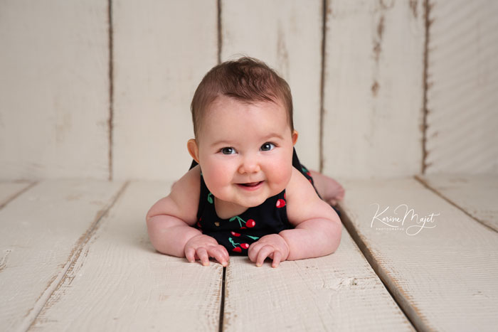petite fille de quatre mois allongée sur le ventre et riant, sur un décor en bois blanc bohême