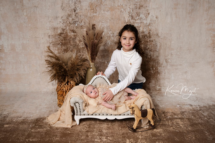 bébé dans un lit vintage avec sa grande sœur pour un shooting naissance avec Karine Majet