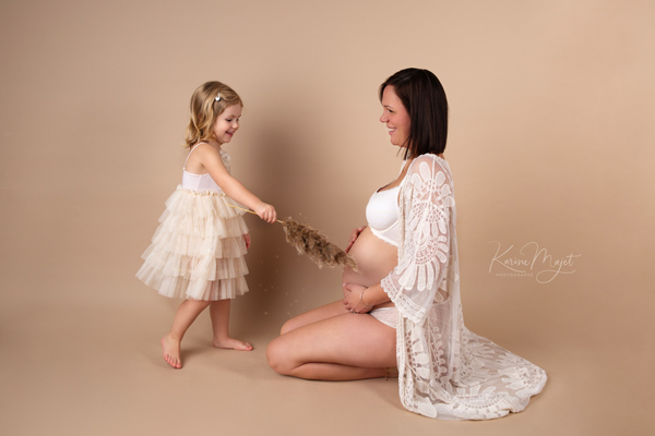 petite fille s'amuse avec une pampa et fait des chatouille sur le ventre de sa maman