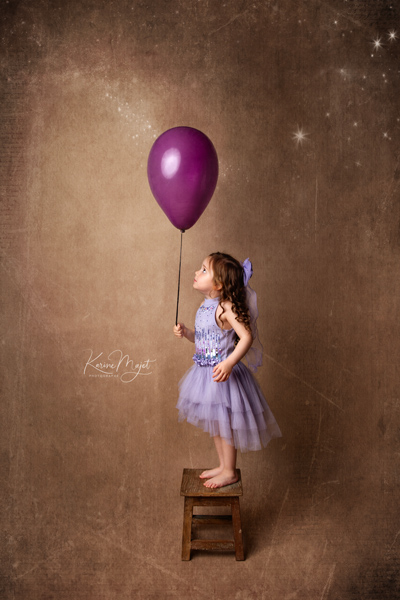 petite fille de 5 ans avec une robe mauve et regarde un grand ballon