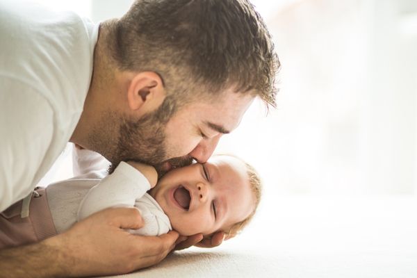 un papa fait des bisous à son bébé qui fait des grands sourires