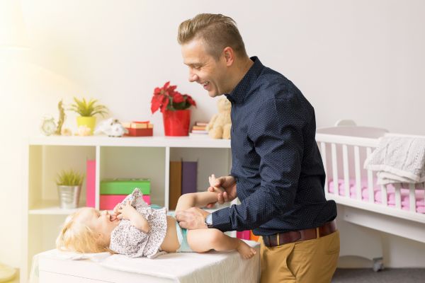 un papa sourit à sa fille pendant qu'il la change