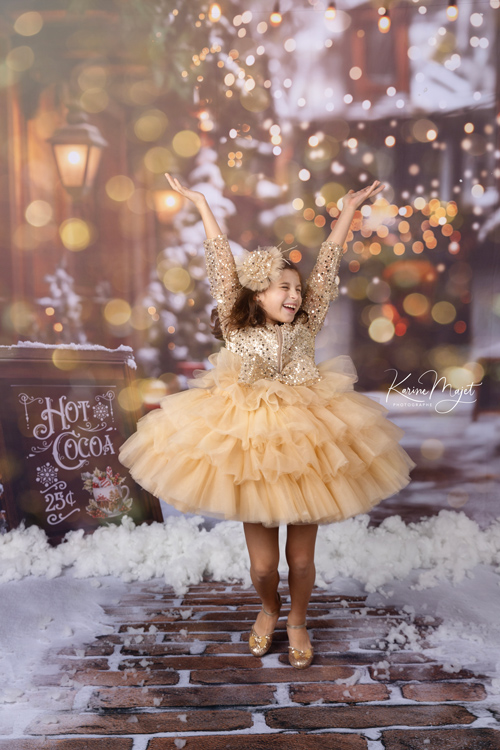 petite fille sautant et souriant pour un shooting de Noël avec une robe dorée